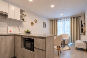 A modern kitchen with built-in appliances, a dining area with a chair and table, and a large window with curtains. - Moderno Loft en Malecón Piscina Gym (Lima)