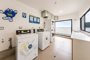 A modern laundry room with two front-loading washing machines, a wall-mounted mascot, and informational posters. - Moderno Loft en Malecón Piscina Gym (Lima)