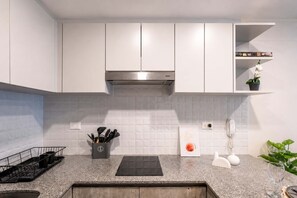 A modern kitchen with white cabinets, a stainless steel range hood, a countertop with a knife block, and a potted plant. - Moderno Loft en Malecón Piscina Gym (Lima)
