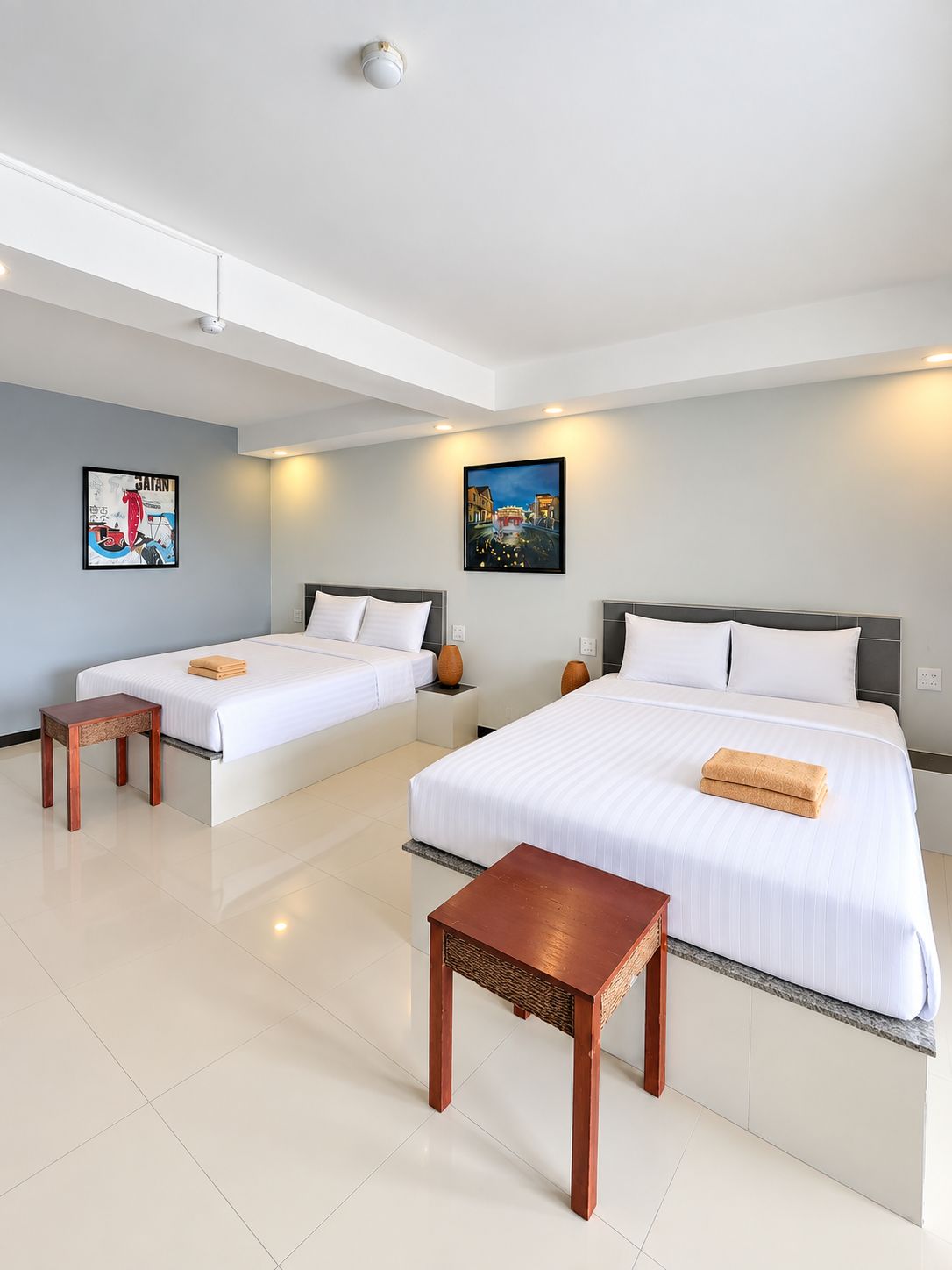 Habitación de hotel con dos camas, una mesita pequeña y obras de arte en las paredes.