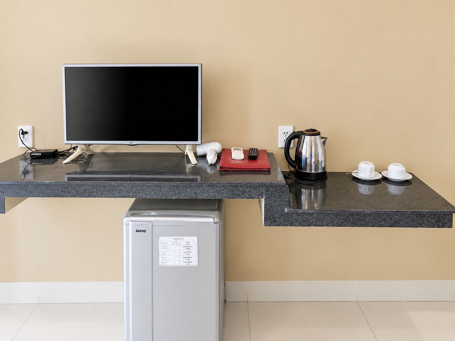 Una kitchenette con una televisión de pantalla plana, cafetera, hervidor y refrigerador.