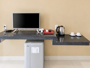 Una kitchenette con una televisión de pantalla plana, cafetera, hervidor y refrigerador.