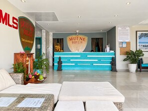 Una zona de recepción con mostrador azul, una estatua de Buda y un cartel que dice 'MUI NE HILLS'.