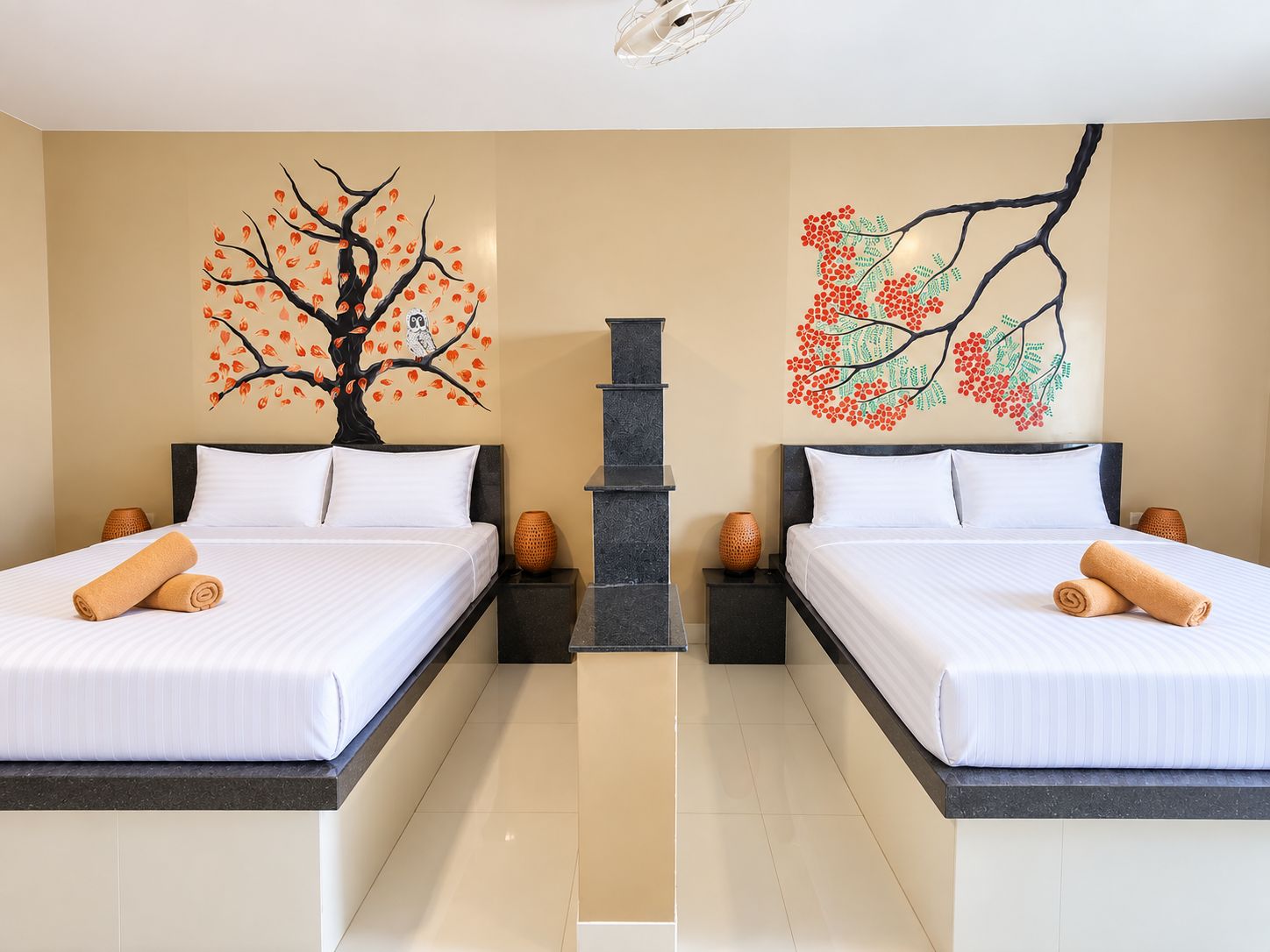 Habitación de hotel con dos camas, un pilar central y arte mural con motivos de árboles.