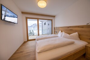 A bedroom with a wooden bed, a television on the wall, and a large window offering a mountain view. - Apartment With Sauna Near ski Resort (Hollersbach im Pinzgau)