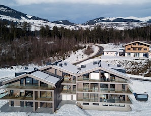 A modern multi-story building with large windows and a flat roof, surrounded by snow-covered mountains and trees. - Apartment With Sauna Near ski Resort (Hollersbach im Pinzgau)