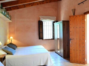 Ein Schlafzimmer mit einem Bett, einem Kleiderschrank, einem Fenster mit Fensterläden und einer Lampe.