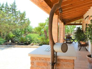 Ein möblierter Patio-Bereich im Freien mit einem Steintisch, umgeben von Blumentöpfen und einer Holzpergola.