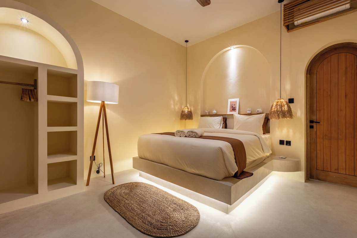 A modern bedroom with a bed, bedside lamps, a wardrobe, and a wooden door.