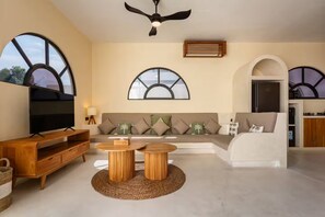 A modern living room with a flat-screen TV, a sofa, two round wooden tables, and a ceiling fan. - Dimora Bali Signature (Badung)