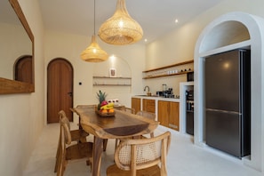 A modern kitchen with a wooden dining table, wicker chairs, and a fruit bowl. - Dimora Bali Signature (Badung)