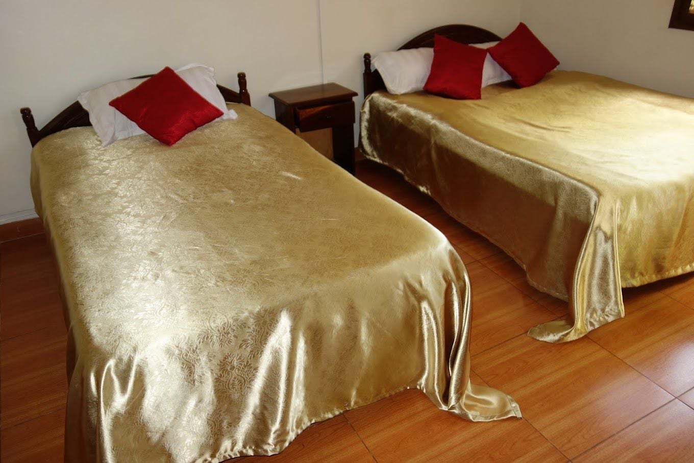 Due letti singoli con telai in legno e cuscini rossi, un comodino in legno e un pavimento piastrellato.