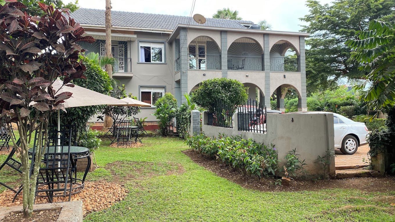 A two-story house with a covered patio, a car parked in front, and a garden with various plants.