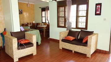 Una habitación con dos sofás de mimbre, una zona de comedor con mesa y sillas, y una ventana con cortinas.