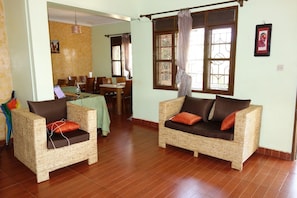 A room with two wicker sofas, a dining area with a table and chairs, and a window with curtains.