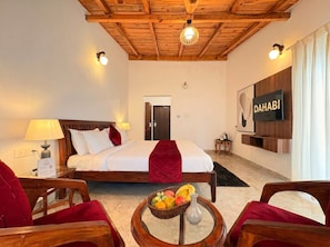 Habitación de hotel con una cama, televisión, escritorio y una cesta de frutas.