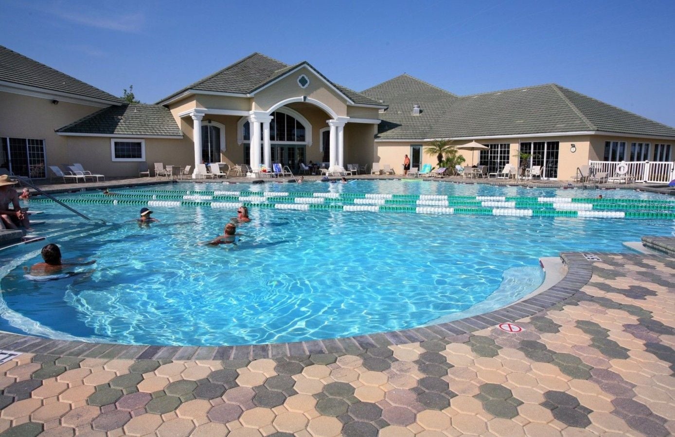 A swimming pool with multiple lanes, lounge chairs, and a covered area with a building in the background.