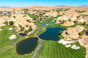 Ein Golfplatz mit mehreren Teichen, einer Brücke und einer Wüstenlandschaft im Hintergrund.