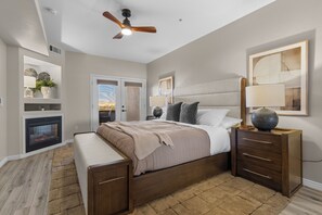 Ein Schlafzimmer mit einem Bett, Nachttischen, einem Deckenventilator, einem Kamin und einem großen Fenster.