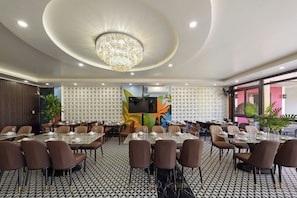A conference room with round tables, chairs, a chandelier, and a large screen.