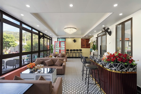 A hotel lobby with a sofa, chairs, a reception desk, and a large window.