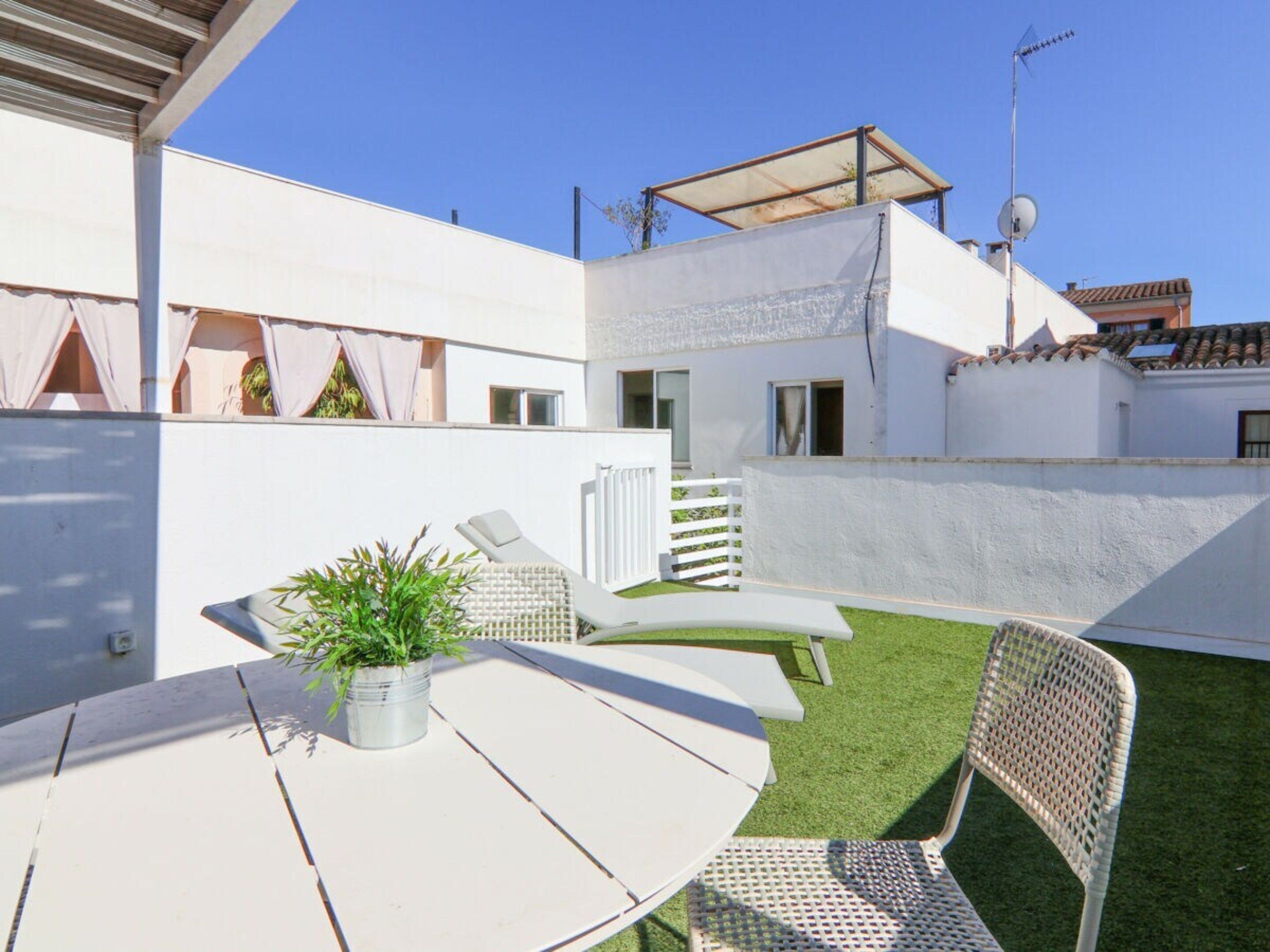 A patio with a white table, two lounge chairs, and a potted plant.