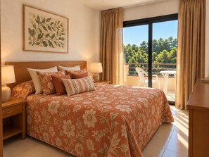 A hotel room with a large bed, two bedside tables, a nightstand, a window with curtains, and a balcony with a table and chairs. - Coastal Family Apartment With Pool (Pals)