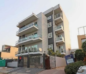 Un edificio residencial de varios pisos con balcones, un acceso con portón y un cartel visible.