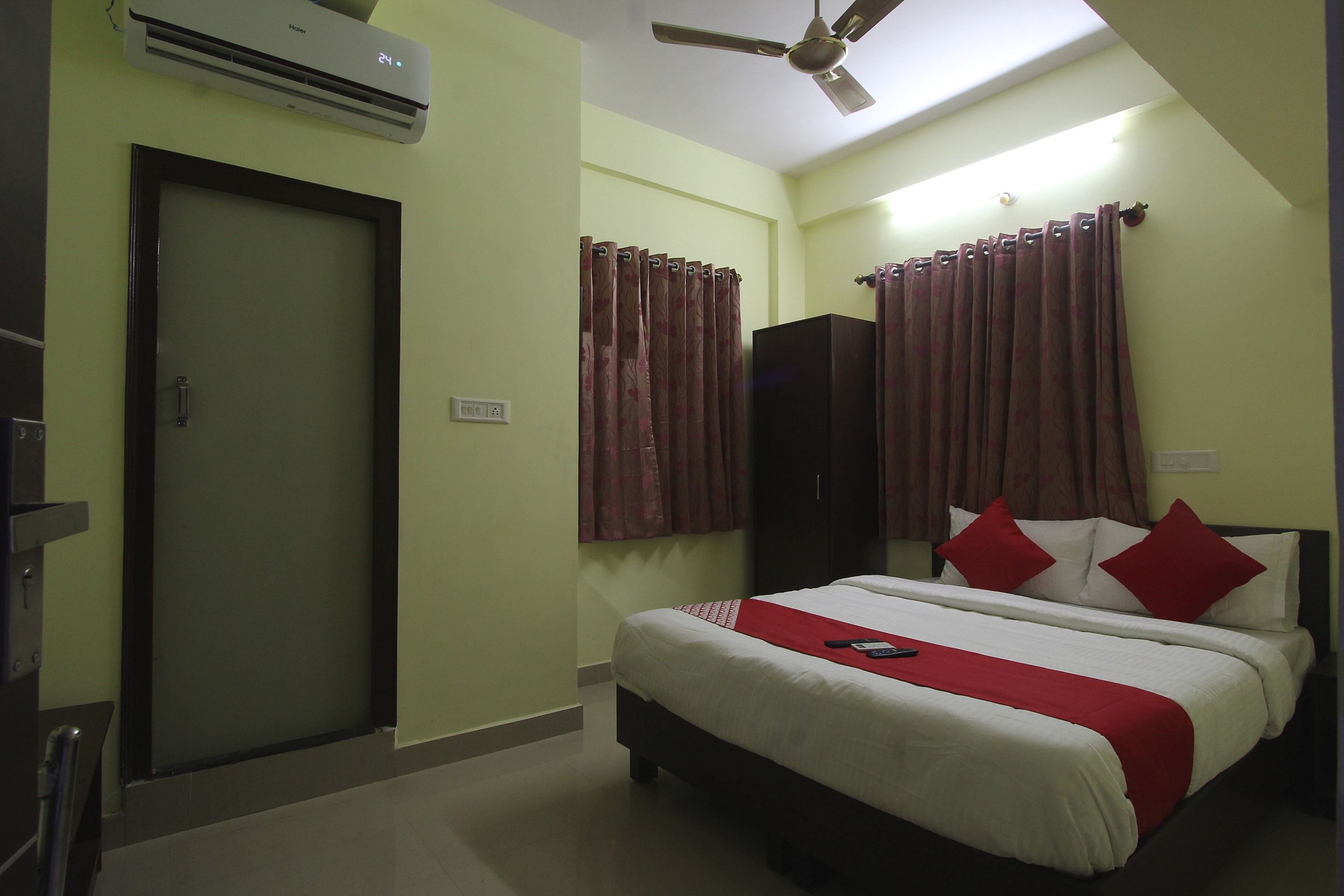 A hotel room with a bed, a wardrobe, an air conditioning unit, a ceiling fan, and a door.