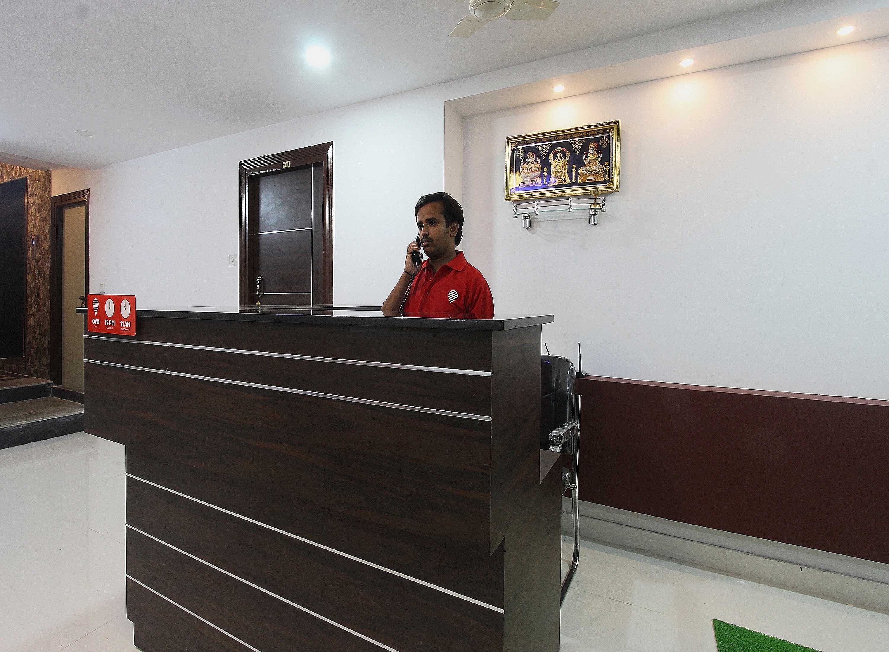 A reception desk with a wooden finish and a glass partition. There is a framed artwork above the desk and a door with a sign on the wall.