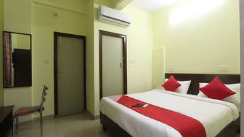 A hotel room with a bed, a chair, a desk, and an air conditioning unit.