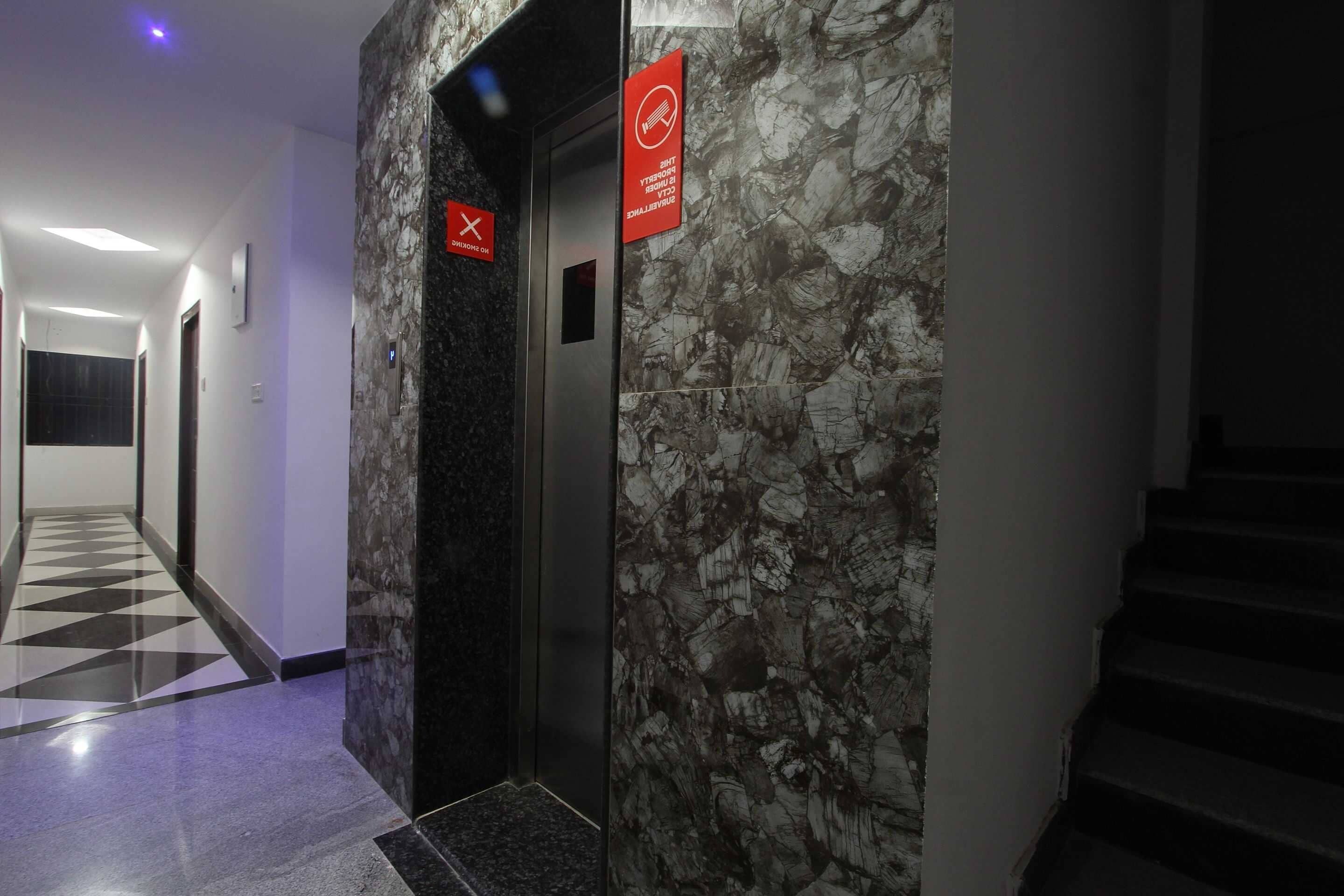 Un pasillo con pared de mármol, un ascensor y una escalera.