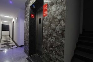 Un pasillo con pared de mármol, un ascensor y una escalera.