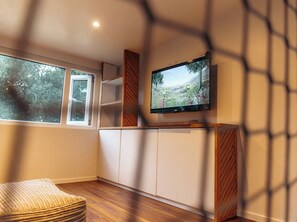Ein Zimmer mit Fernseher an der Wand, einem Fenster und einem Holzschrank.