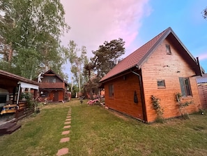A wooden cabin with a red roof, surrounded by a grassy yard and trees. - Holiday Home for 4 People, Dziwnow (Dziwnów)