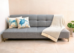 A grey sofa with two decorative pillows, a knitted throw, and a potted plant. - King Bed, Fiber-Optic WiFi for Video Calls, Desk, AC, Laundromat Next Door (Playa del Carmen)