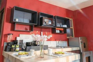 Eine Küche mit roter Wand, schwarzen Schränken und einer Holzarbeitsplatte. Auf der Arbeitsplatte befinden sich Geräte wie eine Kaffeemaschine, ein Toaster und ein Mixer.