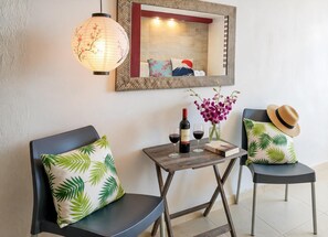 Quarto com duas cadeiras, uma mesa pequena, uma garrafa de vinho, um copo e um vaso com flores.