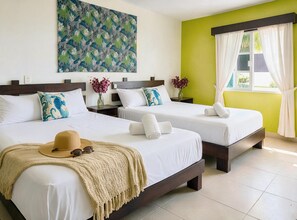 Quarto de hotel com duas camas, uma janela grande com cortinas, um quadro na parede e um chapéu sobre a cama.
