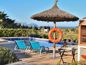 A pool area with a thatched umbrella, lounge chairs, and a lifebuoy. - 1-bedroom Finca (Santa Margalida)