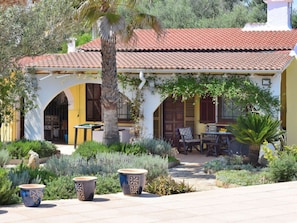 A Mediterranean-style building with a tiled roof, arched doorways, and outdoor seating. - 1-bedroom Finca (Santa Margalida)