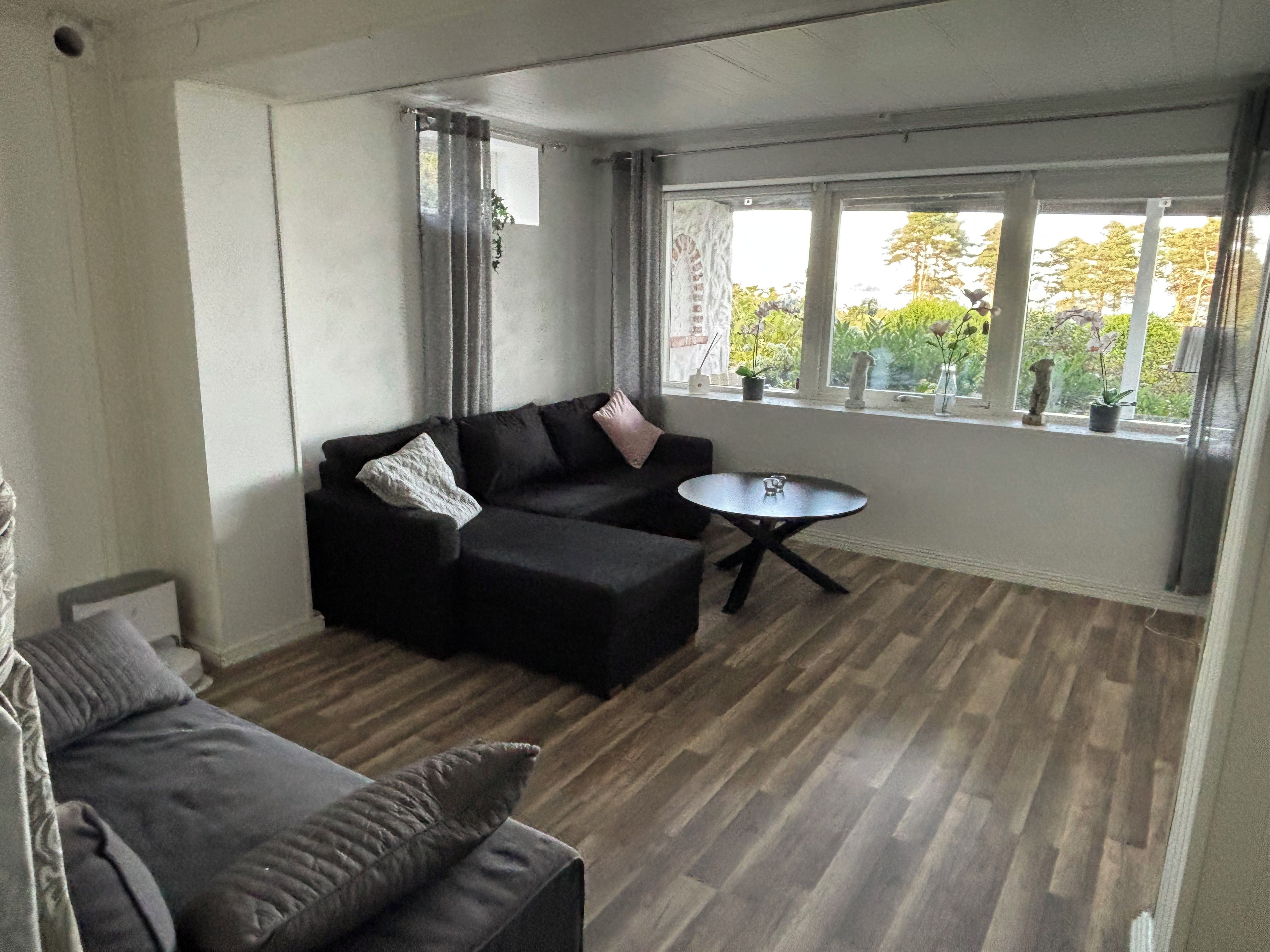 Een moderne woonkamer met een modulaire bank, een ronde salontafel en een groot raam met uitzicht op groen.