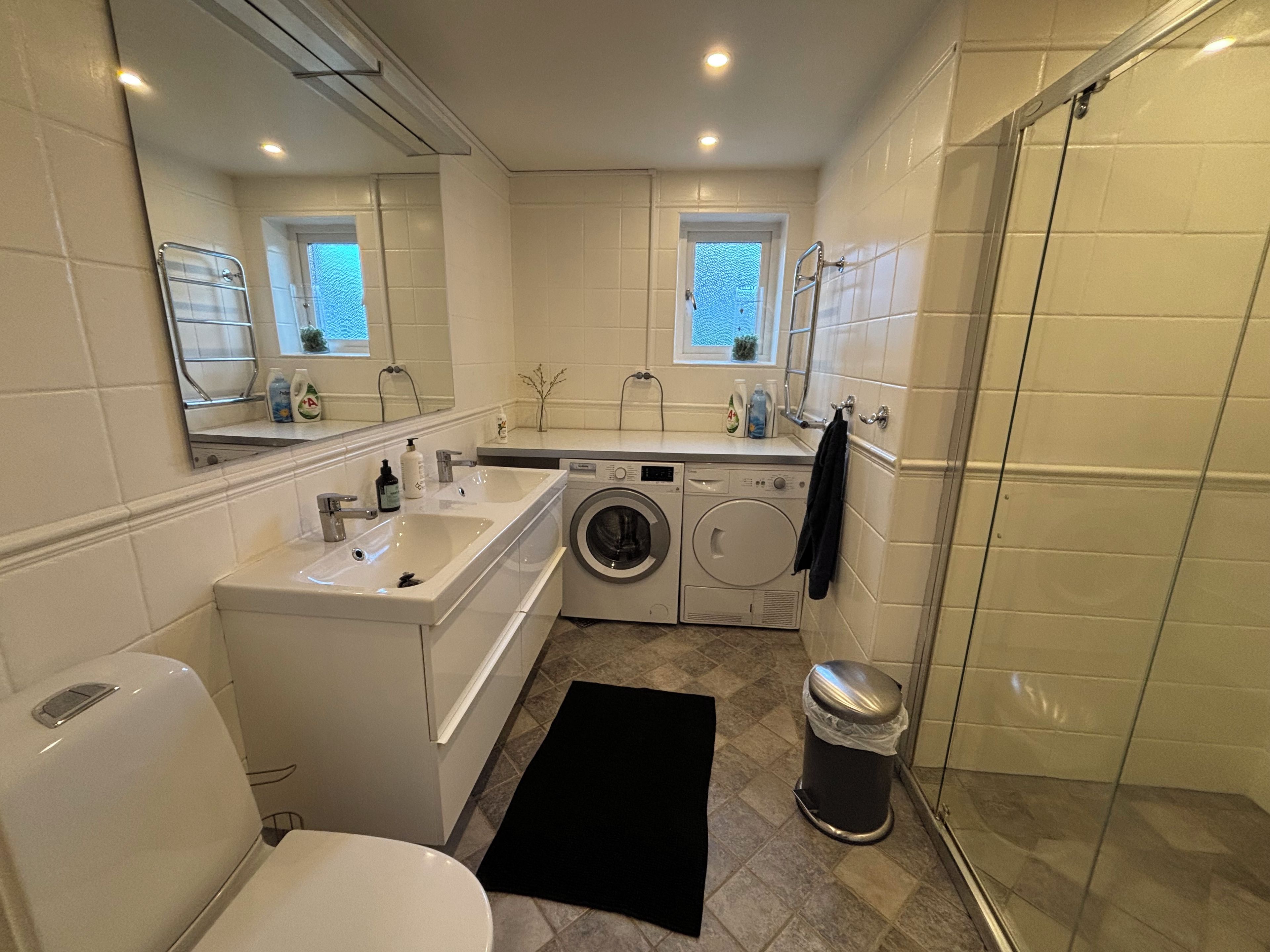 A compact bathroom with a toilet, sink, washing machine, and a shower area.