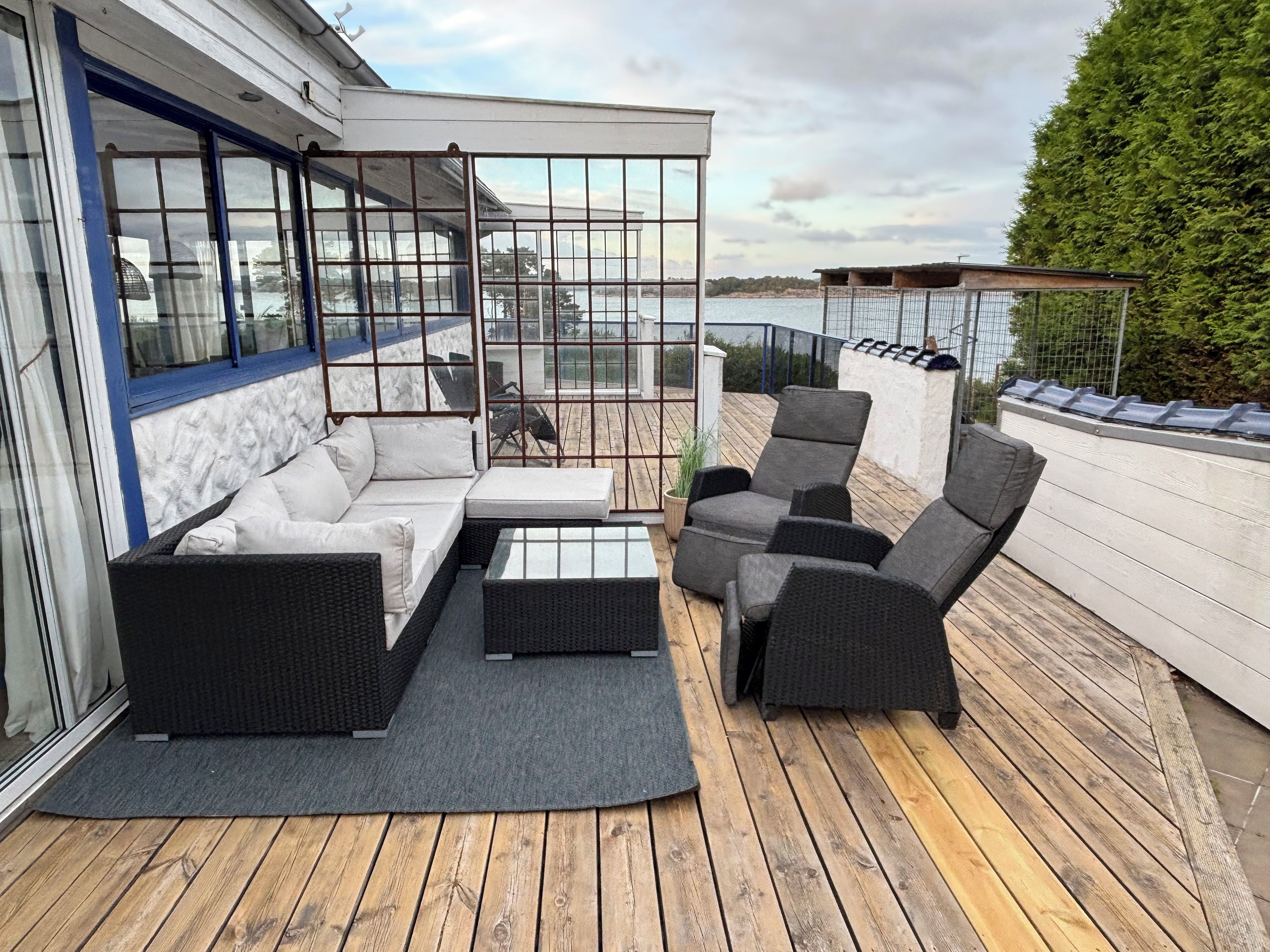 Une terrasse dotée de mobilier d’extérieur, notamment d’un canapé et de fauteuils, et d’une cloison en verre.