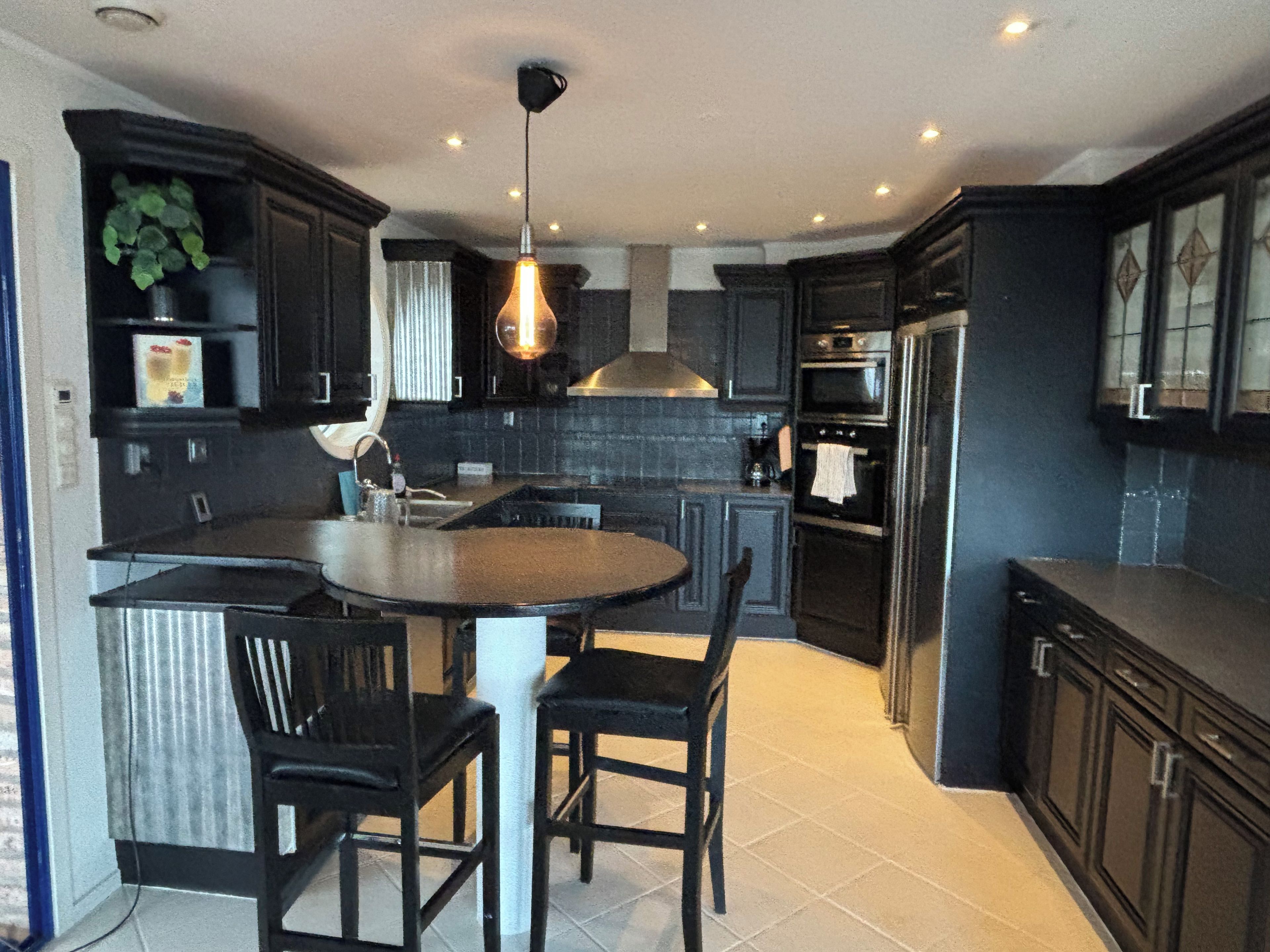 A modern kitchen with dark cabinetry, a central island with chairs, and a hanging light fixture.