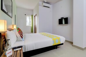 Habitación de hotel con una cama, televisor, ventana con cortinas, equipo de aire acondicionado y un control remoto sobre la mesita de noche.