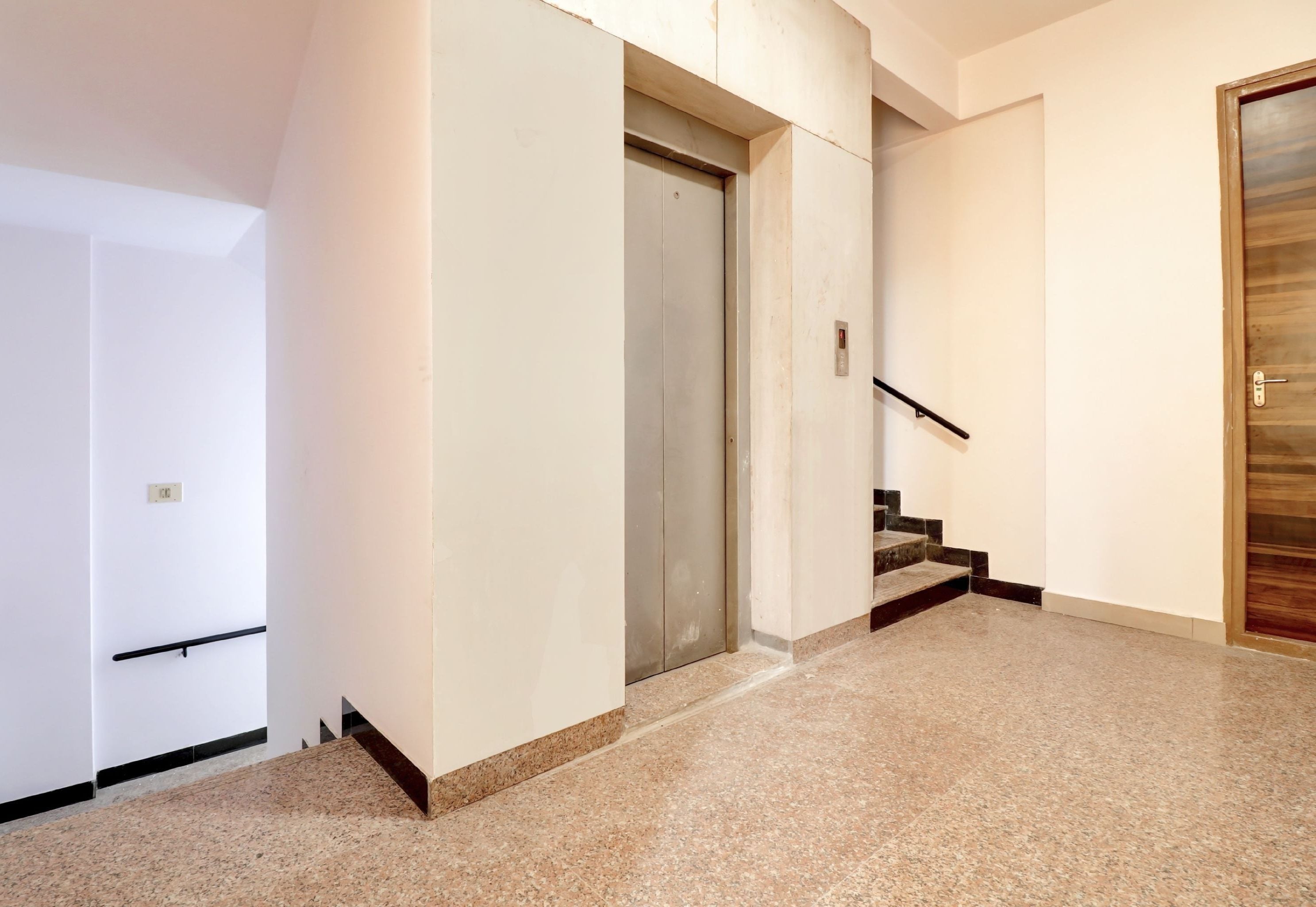 Un pasillo con una puerta, una escalera y un panel de control de ascensor en la pared.