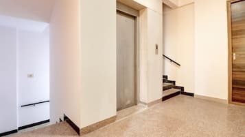 Un pasillo con una puerta, una escalera y un panel de control de ascensor en la pared.