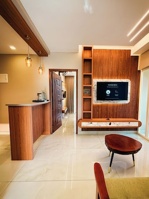 A modern living room with a wooden entertainment unit, a flat-screen TV, and a marble accent wall. - Vaga Castle by Amish Hospitality (Peermade)