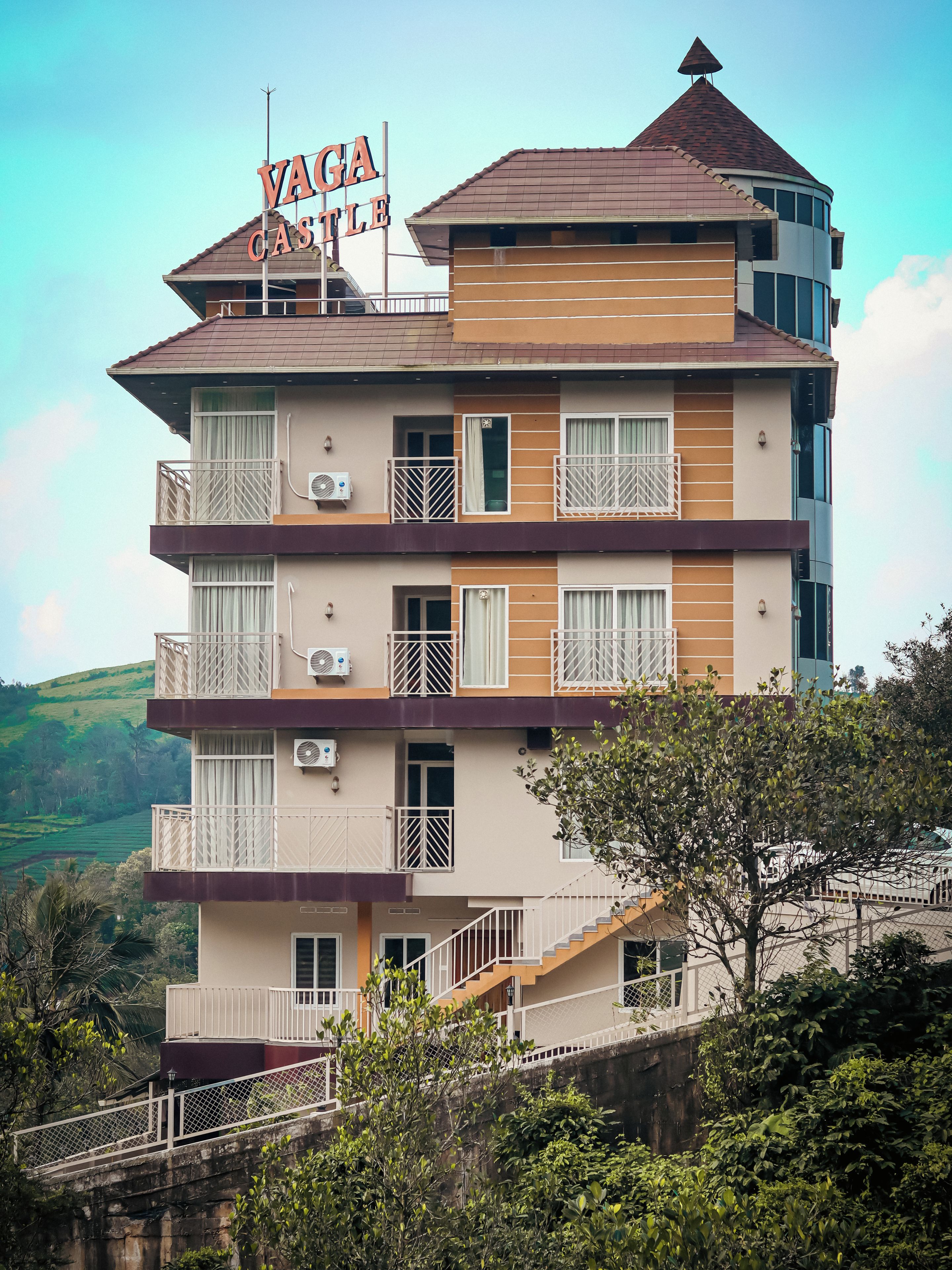 A multi-story building with a sign reading 'Vaga Castle.' It features balconies with railings, air conditioning units, and a staircase leading to the entrance.